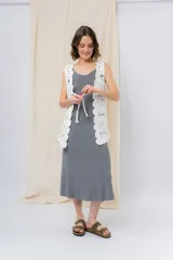 Chaleco tejido calado color crudo, con diseño artesanal, silueta relajada y largo a la cadera. Presenta terminación ondulada y detalle de lazo frontal.