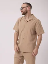 Camisa color beige de lino y poliéster, de manga corta, con cuello solapa y cierre frontal con botones.