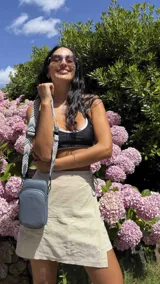 Bandolera pequeña tipo 'phone bag' de símil cuero color rosado pálido, con cierre de cremallera y correa ancha de tela con diseño de chevron en tonos claros.