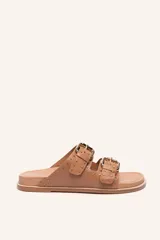 Sandalias bajas color tostado con dos tiras anchas con hebillas doradas y tachas.