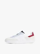 Zapatillas urbanas de corte bajo con exterior de ante blanco, detalles en gris y azul celeste, y refuerzo en el talón de cuero burdeos. Presentan el logo de la marca bordado en el lateral y en la parte trasera.