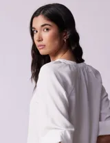 Blusa blanca de gasa marca Sioni, con cuello a la base y escote en V. Tiene abertura central con botones y mangas 3/4 con terminación fruncida.