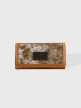 Billetera de cuero color camel con solapa frontal de cuero con pelo en tonos marrón y blanco. Incluye un parche de cuero marrón oscuro con el logo de la marca.