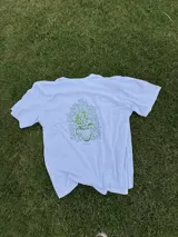 Remera blanca de algodón con cuello redondo y mangas cortas. Estampado en la espalda con un jarrón con flores y la palabra 'tuya'.