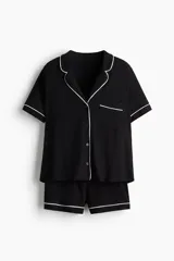 Pijama corto de dos piezas color negro, en punto suave con ribetes blancos en contraste. Camisa de manga corta con cuello abierto, botones al frente y bolsillo superior abierto. Short con elástico en la cintura.