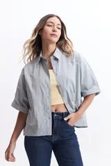 Camisa celeste de corte amplio, con cuello clásico, cierre frontal con botones y mangas cortas con dobladillo.