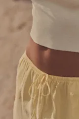 Pantalón de mujer color amarillo pálido, de corte ancho y tejido fluido. Tiene tiro medio, cintura elástica ajustable con cordones, bolsillos laterales y falsos bolsillos de vivo en la espalda.