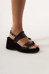 Sandalias de cuero color marrón con plataforma y taco de cuña forrado en gamuza negra. Presentan dos tiras anchas con detalle de pespuntes en el borde y hebilla dorada en la tira del tobillo.
