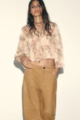 Camisa con estampado animal print en tonos beige y marrón, con cuello solapa y escote pico. Manga larga con capas en mismo tejido y bajo acabado en volantes. Cierre frontal con botones y lazada.