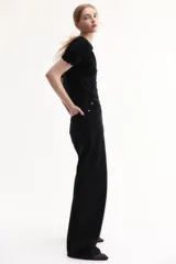 Saco corto negro de punto fino suave con cuello redondo, mangas cortas y botonadura frontal. Tiene ribete festoneado en tapeta, mangas y bajo.