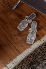 Sandalias negras de cuero con tira ancha sobre el empeine y tira entre los dedos, ambas adornadas con apliques metálicos plateados.