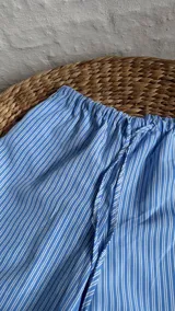 Pantalón celeste con rayas verticales blancas, de corte recto y cintura elastizada con cordón ajustable.