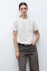 Blusa de manga corta color crudo, con cuello redondo y diseño de encaje bordado floral.