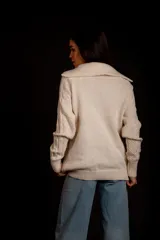 Buzo de punto color crema con cierre metálico y cuello alto.