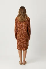 Vestido camisero corto color marrón con estampado abstracto en tonos naranja. Tiene cuello camisero, cierre frontal con botones y mangas largas.