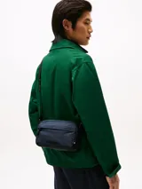 Bandolera Tommy Hilfiger azul marino con correa ajustable de tejido trenzado, cierre de cremallera, bolsillo exterior con cremallera y logo texturizado en la parte delantera.