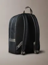 Mochila de piel sintética granulada color negro, con asa superior de tela gris y correas ajustables. Presenta un bolsillo frontal con cierre y el monograma de Calvin Klein en relieve en la parte inferior.