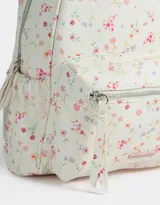 Mochila pequeña de cuerina color crema con estampado de flores pequeñas en tonos rosa, naranja y celeste. Tiene un bolsillo frontal con cierre, correas regulables, manija superior, cierre superior y bolsillos laterales.