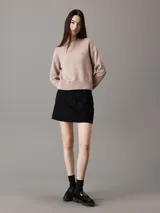 Sweater color beige de punto de algodón orgánico, con cuello redondo alto, mangas largas y logo bordado en el pecho.