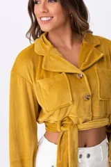 Campera corta color mostaza, con cuello tipo camisa, cierre frontal con botones, dos bolsillos de parche en el pecho y lazo para atar en la cintura.