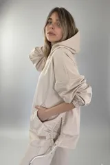 Canguro beige oversize de tejido suave con capucha, cordones ajustables y bolsillo tipo canguro.