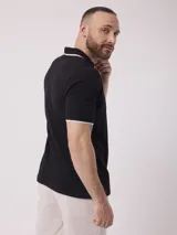 Remera negra de corte clásico con cuello polo y mangas cortas con ribete blanco. Confeccionada en tejido liso de mezcla de algodón y poliéster.