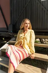 Camisa amarilla con bordado inglés, escote en V, mangas largas abullonadas con puños elásticos y lazos decorativos en el frente.