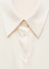 Camisa color crema de tejido fluido con textura y acabado satinado. Tiene cuello clásico, cierre de botones frontal y mangas largas con puños abotonados.