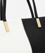 Cartera shoulder mediana de cuero sintético, con diseño bicolor blanco y negro y detalles metálicos dorados.