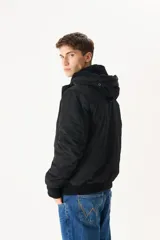 Campera negra con capucha con borde de piel sintética color beige, cierre frontal con cremallera y botones a presión, bolsillos laterales con solapa y puños acanalados.