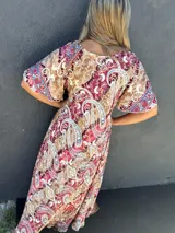 Vestido largo de seda con estampado paisley en tonos marrón, rojo oscuro y azul. Presenta escote en V y mangas cortas con volado.