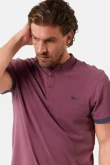 Remera de manga corta color azul grisáceo con cuello mao y tapeta de botones. Los puños de las mangas y el cuello son de color azul marino contrastante. Presenta un pequeño logo bordado en el pecho.