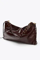 Bolso de hombro alargado color marrón oscuro, con detalle de pasados metálicos en los laterales y asa trenzada. Doble bolsillo interior con cremallera. Cierre mediante botón imantado.