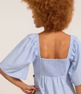 Vestido corto evasê de viscolino color crudo, con escote en V, mangas cortas amplias, recorte cut-out en los laterales de la cintura y volado en el ruedo.