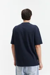 Remera beige de manga corta con textura y corte oversize. Presenta un pequeño bordado en relieve en el pecho.