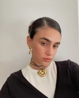 Collar con dije dorado irregular con agujero central, colgando de cordón negro ajustable.