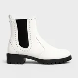 Bota Chelsea blanca de cuero sintético con elástico lateral negro adornado con tachas plateadas. Tiene suela track negra y taco bajo.