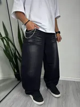 Pantalón de jean negro con lavado gastado, corte ancho y cadena metálica colgando del bolsillo.