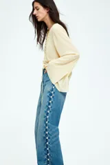 Blusa color crema de gasa con escote en V y cordones cruzados. Tiene mangas largas acampanadas y pliegues en la cintura.