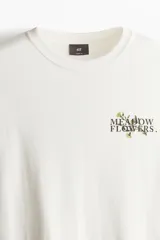 Remera color crema de corte holgado con estampado de flores y texto en el pecho.
