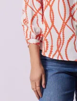 Blusa estampada blanca con diseño de cadenas y círculos color naranja. Cuello redondo con escote en V y lazo de ajuste. Manga 3/4.