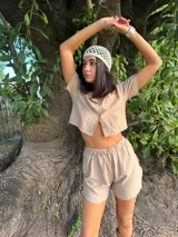 Set de dos piezas color beige compuesto por una camisa de manga corta tipo crop con botones frontales y cuello solapa, y un short de tiro alto con cintura elástica.