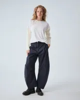 Pantalón de gabardina azul marino, de tiro medio y largo hasta los tobillos. Tiene cierre metálico y broche níquel en la cartera, además de bolsillos laterales. Silueta comba con piernas anchas y sutilmente curvadas, logradas a través de pinzas en el ruedo y a la altura de la rodilla. En la espalda bolsillos ojal con broches metálicos.