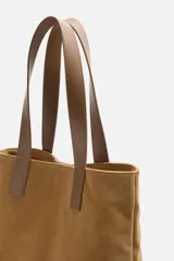 Bolso tipo shopper color marrón claro, fabricado en cuero con acabado serraje. Tiene doble asa de mano de cuero y un bolsillo interior con cierre.