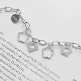 Pulsera plateada de acero quirúrgico con cadena de eslabones y dijes colgantes: moneda, flores caladas y cuadrado con círculo.