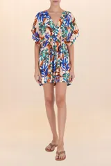 Vestido corto de manga mariposa, escote en V y cintura ajustada con frunce. Presenta un estampado botánico vibrante sobre fondo blanco, con hojas en tonos azules, naranjas y verdes.