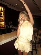 Vestido corto color crema con cuello halter y espalda descubierta. Presenta cintura elastizada y falda con volados.