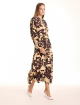 Vestido maxi de crepe estampado con flores grandes en tonos beige y marrón oscuro. Presenta escote en V con botones, mangas largas anchas con botón en los puños, y cintura con pasadores y cordón de ajuste.