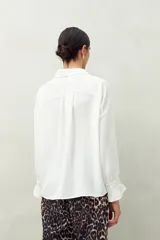 Camisa negra de manga larga con cuello clásico y botones frontales. El tejido presenta una textura arrugada o plisada, y los puños tienen un detalle fruncido o elástico.