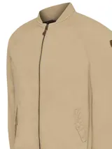 Campera bomber color beige de algodón orgánico con spandex, corte regular, cuello, puños y pretina acanalados, cierre frontal, bolsillos delanteros con solapa y broches ocultos, bolsillos internos y forro de franela.